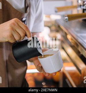 Il barista versa il latte nel caffè Foto Stock