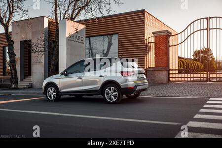 silver SEAT Arona parcheggiata vicino a un moderno edificio a un piano. Vista posteriore di tre quarti del crossover in berlina spagnola al tramonto. Foto Stock