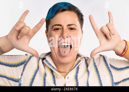 Persona giocosa androgina con i capelli blu che sporgono la lingua mostrando piercing - braccialetto orgoglio LGBT, espressione gioiosa, divertente e vibrante - incluso a. Foto Stock