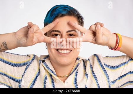 Persona androgina sorridente con capelli blu che fa un gesto giocoso della mano - braccialetto orgoglio LGBT, espressione felice, inclusivo e divertente - vibrante e colorato Foto Stock