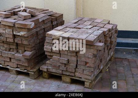 Mattoni usati impilati su pallet di legno vicino alla parete di un edificio. Primo piano. Foto Stock