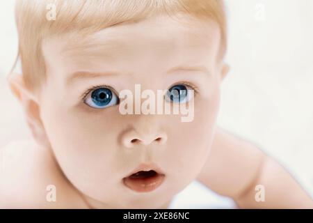 Il bambino con gli occhi blu guarda innocentemente e curiosamente, irradiando felicità e salute, catturando la meraviglia dell'infanzia in un ritratto in studio Foto Stock