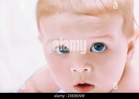 Dolce bimbo con occhi azzurri ipnotici che sdraiati tranquillamente su un letto accogliente. Osservando con un'espressione curiosa e innocente. Irradiando felicità e salute Foto Stock