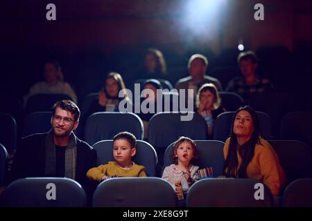 Una famiglia moderna ama trascorrere momenti di qualità insieme al cinema, viziandosi con popcorn mentre guarda un film con i propri figli Foto Stock