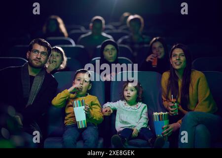 Una famiglia moderna ama trascorrere momenti di qualità insieme al cinema, viziandosi con popcorn mentre guarda un film con i propri figli Foto Stock
