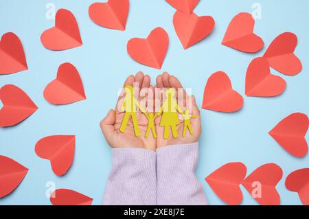 La mano della donna che tiene la carta tagliata famiglia con il bambino, sfondo blu Foto Stock