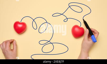 Due cuori rossi su sfondo giallo, la mano di una donna disegna una traiettoria Foto Stock