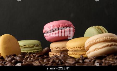 Pila di macaron multicolore su uno sfondo di chicchi di caffè, sfondo nero Foto Stock