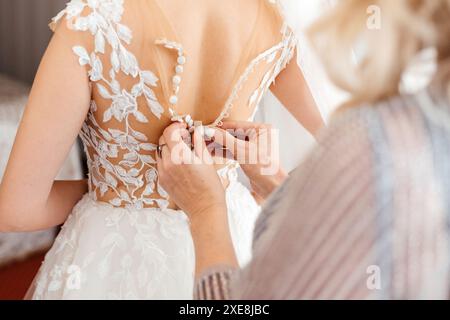 Madre che aiuta la sposa con abito da sposa, preparazione per il giorno di nozze prima della cerimonia Foto Stock