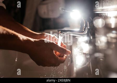 Primo piano di un giovane uomo caucasico che si lava le mani nel lavandino del bagno Foto Stock