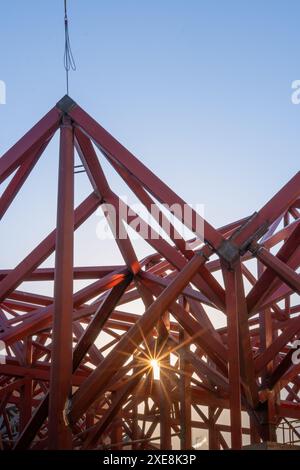 Dettagli di travi metalliche rosse e una gru blu in una costruzione moderna contro un cielo azzurro. Foto Stock