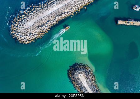 una nave che naviga all'ingresso di un porto protetto da una frangiflutti, vista dall'alto aerea con un drone. Foto Stock