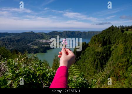 Donna che tiene un fiore di fronte a Lagoa das Sete Cidades. Isola di Sao Miguel, Azzorre Portogallo Foto Stock