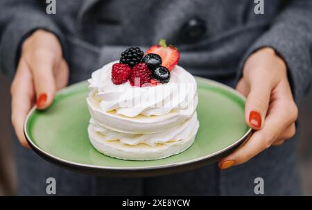 Torta di meringa Pavlova con frutti di bosco freschi su un piatto in mani femminili Foto Stock