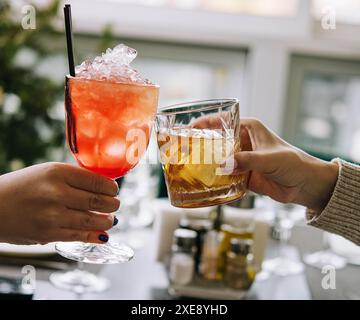 Gli amici brindano con bicchieri di whisky e cocktail di fragole Foto Stock