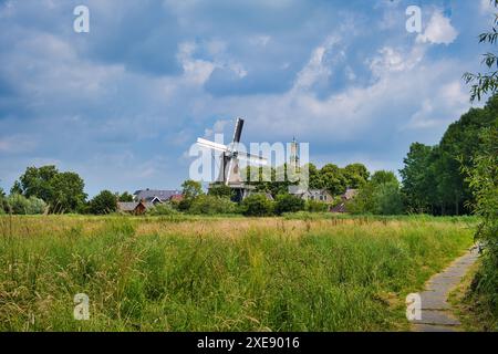 Tipico scenario olandese: Un piccolo villaggio con un mulino a vento, torre della chiesa, campo agricolo, alberi e cielo nuvoloso. Spijk, provincia di Groninga Foto Stock