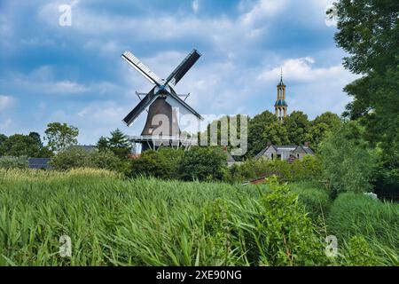 Tipico scenario olandese: Un villaggio con un mulino a vento, una torre di chiesa, un campo agricolo, alberi e un cielo nuvoloso. Spijk, provincia di Groninga Foto Stock