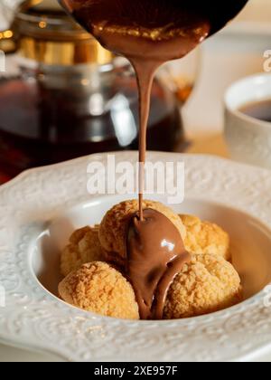 Il cioccolato fuso viene versato sui profiteroles Foto Stock