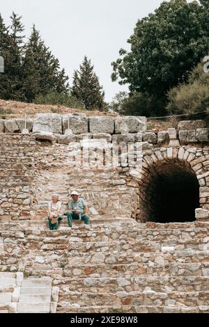 Due persone - turisti - sedevano nelle tribune di un teatro tra le rovine dell'antica città di Efeso a Türkiye in una giornata nuvolosa, un classico viaggio turistico. Foto Stock