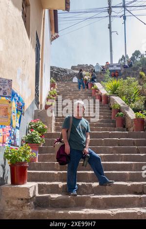 Cusco, Perú; 12 agosto 2023: L'uomo bianco posa su diversi gradini con i fiori in vaso Foto Stock