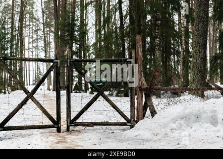 Vecchio cancello in legno impigliato con filo spinato di ferro. Sullo sfondo di una foresta invernale. Foto Stock
