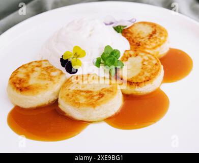 Frittelle dolci con panna acida e marmellata su un piatto bianco Foto Stock