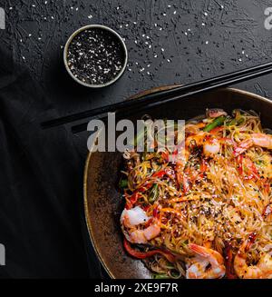 Mescolare gli spaghetti con verdure e gamberetti nel recipiente nero Foto Stock