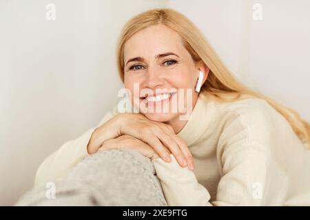 Donna che sorride con gli auricolari in maglione bianco Foto Stock