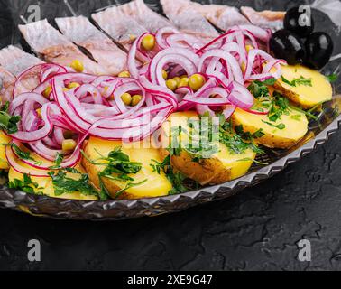 Fettine di aringhe con patate al forno e cipolle marinate su un piatto di vetro Foto Stock