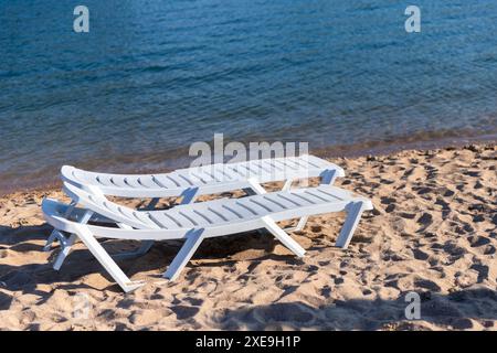 Due lettini bianchi in plastica si trovano su una spiaggia sabbiosa in una giornata di sole Foto Stock