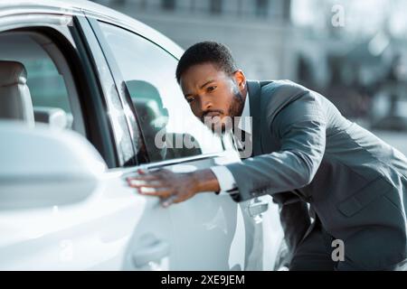 Uomo d'affari che ispeziona la White Sedan Car durante il giorno Foto Stock