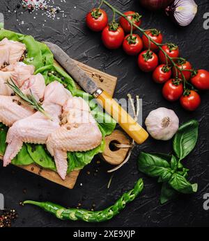 Ali di pollo crude con ingredienti per cucinare su un tagliere di legno su sfondo di pietra scura Foto Stock