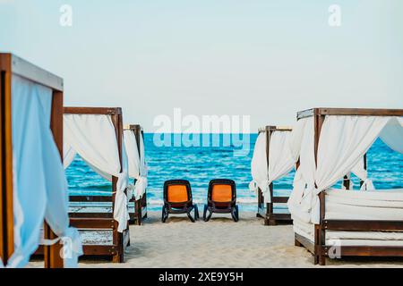 Una fila di cabine bianche con sedie a sdraio sorge su una spiaggia sabbiosa, che offre una tregua dal sole Foto Stock