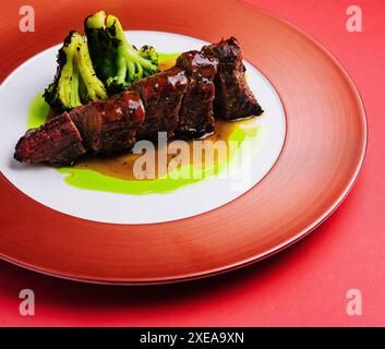 Maiale arrosto con salsa e broccoli sul piatto rosso Foto Stock