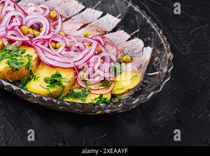 Fettine di aringhe con patate al forno e cipolle marinate su un piatto di vetro Foto Stock