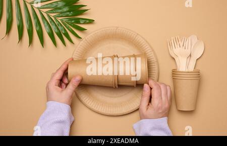 Piatti e tazze di carta, cucchiai e forchette di legno su sfondo beige, vista dall'alto Foto Stock