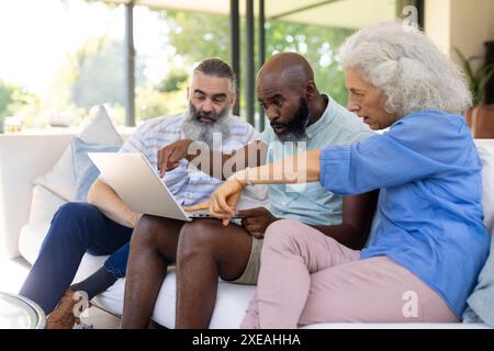 A casa, un gruppo di amici seduto sul divano, usando un computer portatile e discutendo qualcosa insieme Foto Stock