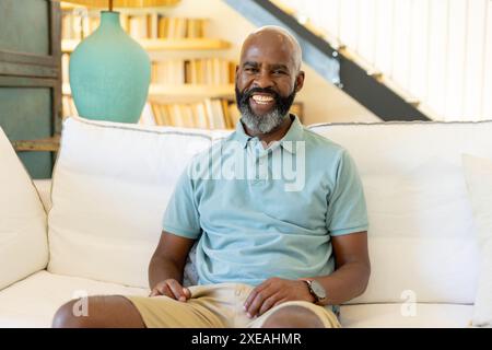 A casa, un uomo sorridente seduto sul divano di casa, godendosi momenti di relax in casa Foto Stock