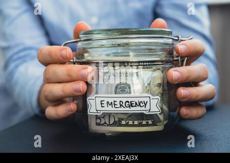 Mani femminili che risparmiano denaro in vasetti di vetro pieni di banconote in dollari. Trascrizione DI EMERGENZA davanti al vaso. Gestione personale Foto Stock