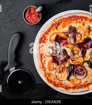 Pizza sul tagliere con taglierina nelle vicinanze, vista dall'alto Foto Stock