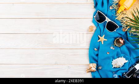Conchiglie, stelle marine, occhiali da sole, bussola, macchina fotografica e cappello di paglia su tessuto blu e tavole bianche vuote Foto Stock