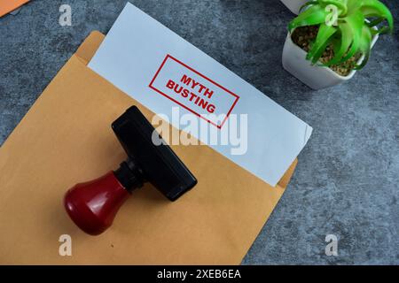 Graffa in gomma con manico rosso e testo con busting Myth sopra una busta marrone isolata su sfondo di legno Foto Stock