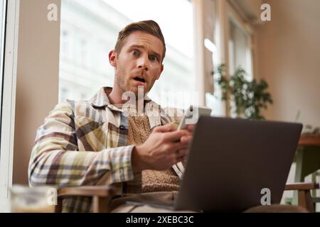 Immagine di un uomo dal volto scioccato e preoccupato, dopo aver letto notizie terribili al telefono. Uomo adulto al bar, seduto in un bar con Foto Stock