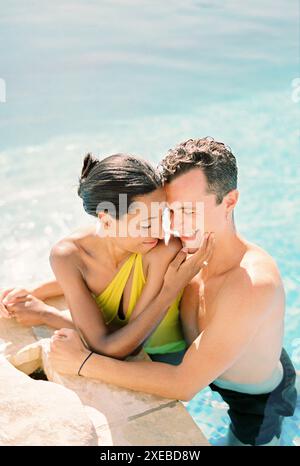 Un uomo sorridente abbraccia la donna, toccando la fronte mentre si è in piscina e appoggiati lateralmente Foto Stock