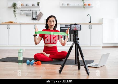 Donna che conduce lezioni di fitness online con banda di resistenza Foto Stock