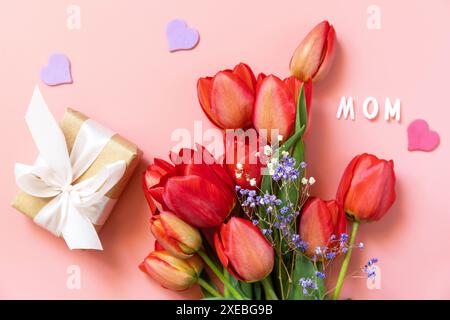 Tulipani rossi con scatola regalo e cuori piccoli, testo scritto a mano dalla mamma su sfondo rosa pastello con spazio vuoto. Foto Stock