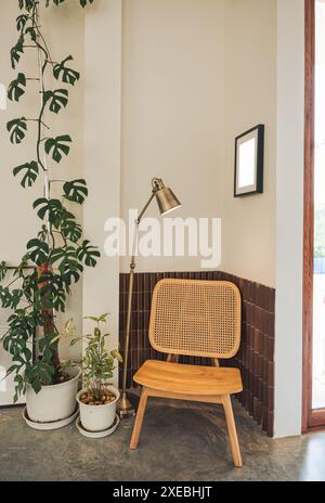 Design retrò degli interni della casa con sedia in tessuto, pianta domestica in vaso, lampada da terra e cornice a quadri sulla parete Foto Stock