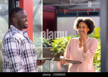 Persone aziendali sorridenti che tengono in mano tablet e si impegnano in conversazioni occasionali all'aperto Foto Stock