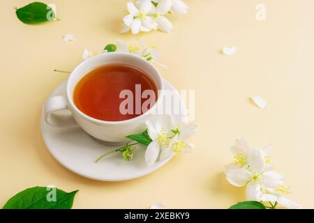 Una tazza di tè e fiori di gelsomino sullo sfondo beige. Vista dall'alto, copia spazio. Foto Stock