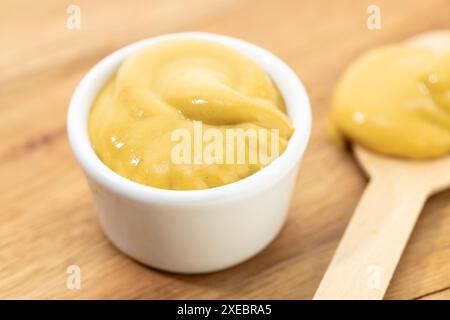 Primo piano della salsa di senape nel recipiente e cucchiaio sul tavolo di legno Foto Stock
